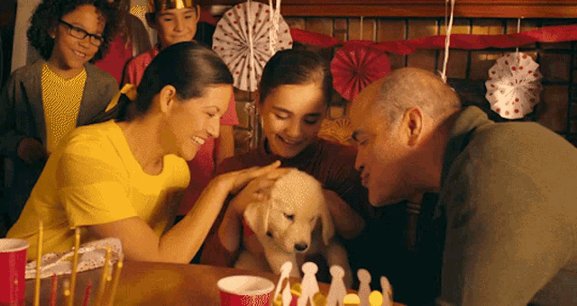a family celebrates a birthday with a puppy in front of a cake