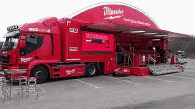a red milwaukee truck is parked in a parking lot with a trailer attached to it .