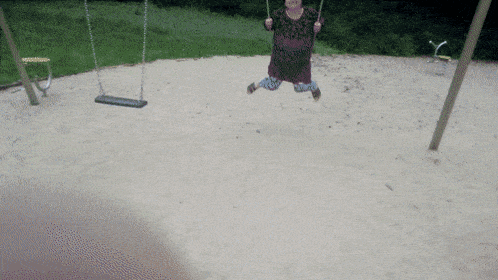 a woman in a purple shirt is swinging in a playground