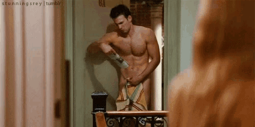 a shirtless man is wrapped in a towel and standing in front of a door .