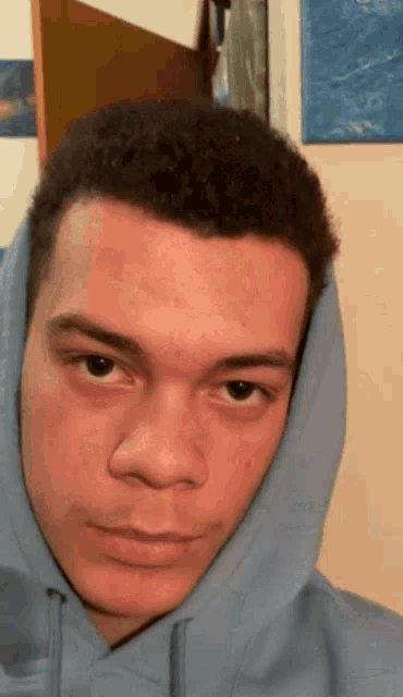 a young man wearing a blue hoodie looks at the camera with a serious look on his face