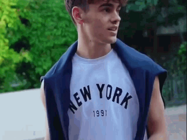 a young man wearing a new york t-shirt is standing on a sidewalk .