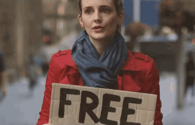 a woman in a red jacket holds a cardboard sign that says free