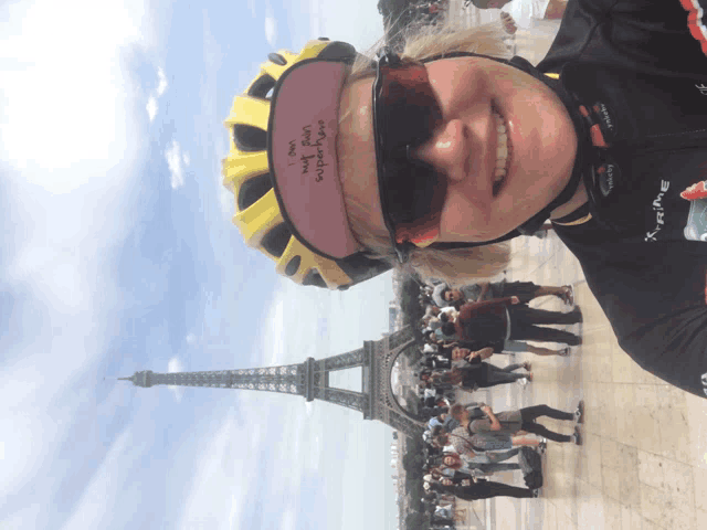 a woman wearing a yellow helmet and sunglasses stands in front of the eiffel tower in paris