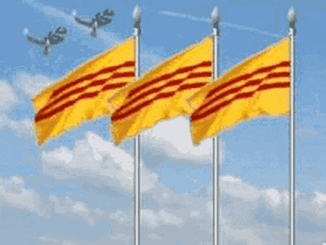 three yellow flags with red stripes are flying in the wind against a blue sky