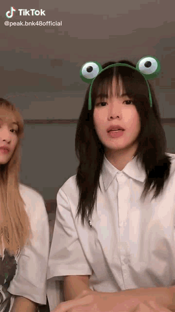 a girl wearing a frog headband is standing next to another girl wearing a white shirt