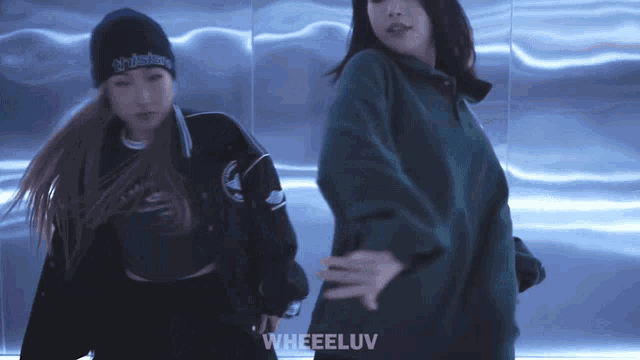 two women are dancing in front of a wall that says wheeluv