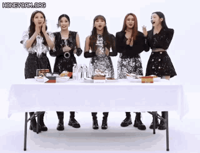 a group of girls are standing around a table with a white tablecloth .
