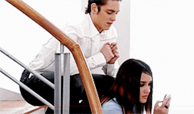 a man and a woman are sitting on a set of stairs looking at their cell phones