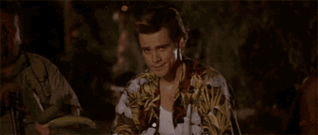 a man in a hawaiian shirt is sitting at a table with a cucumber .