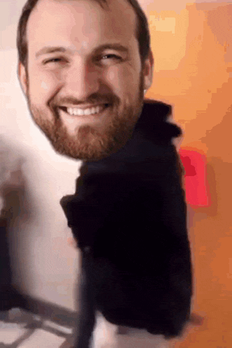a man with a beard is smiling in front of an orange wall