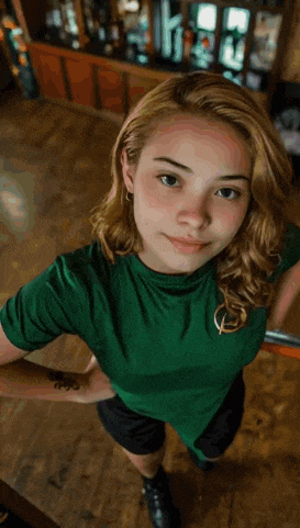 a woman in a green shirt and black shorts is waving at the camera