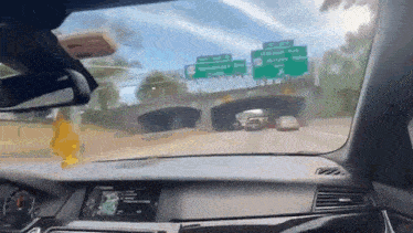 a car is driving down a highway under a bridge with a green sign above it .