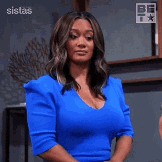 a woman in a blue dress is standing in a room with her hands folded .