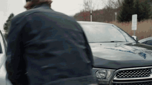a man in a black jacket is standing in front of a black car