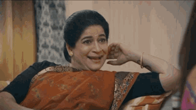 a woman in a saree is sitting on a couch and making a funny face