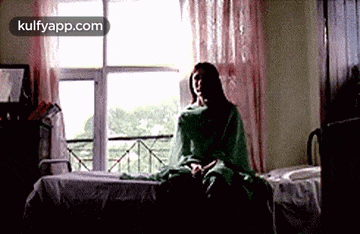 a woman is sitting on a bed in a room with a window .