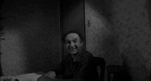 a man is sitting at a table in a black and white photo with a child peeking out of a door behind him .