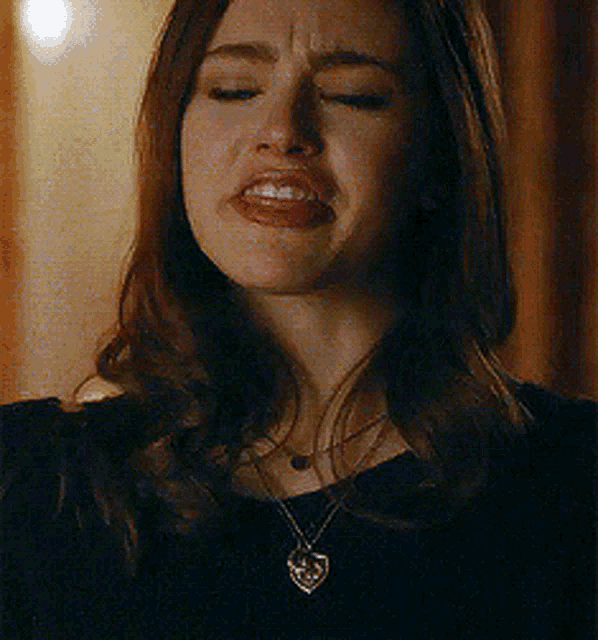 a woman wearing a heart shaped necklace is crying .