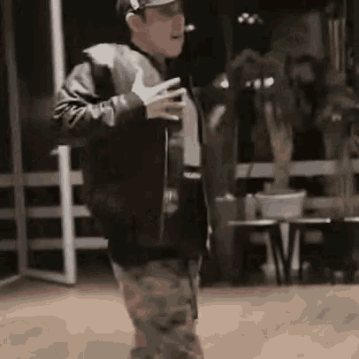 a man is dancing in a room wearing a hat and a leather jacket .