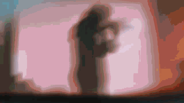 a silhouette of a man and a woman standing next to each other in front of a pink wall .