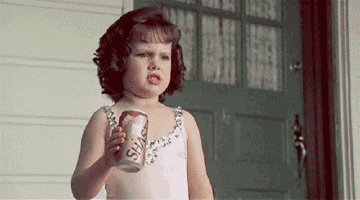 a little girl is holding a can of soda and making a face