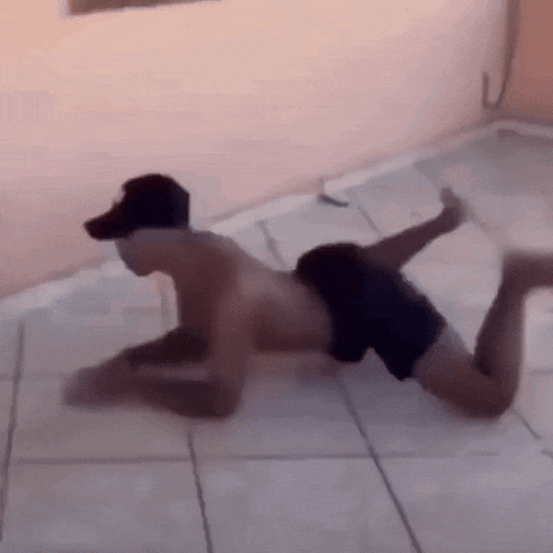 a man without a shirt is crawling on the floor while another man watches .