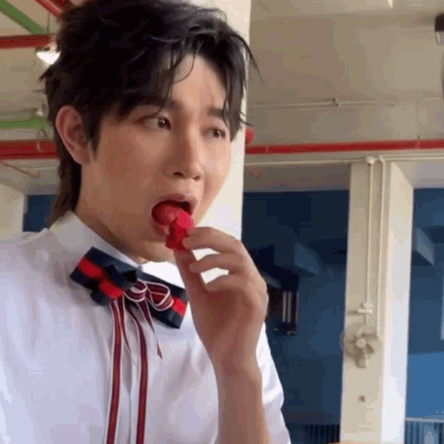 a man wearing a bow tie is eating a red candy