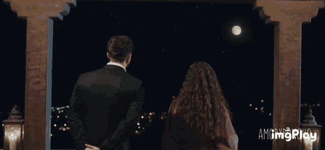 a man and a woman are looking out a window at the moon