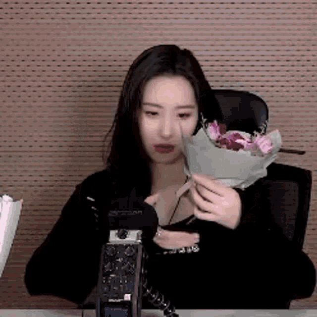 a woman is holding a bouquet of flowers in front of a microphone while sitting at a desk .