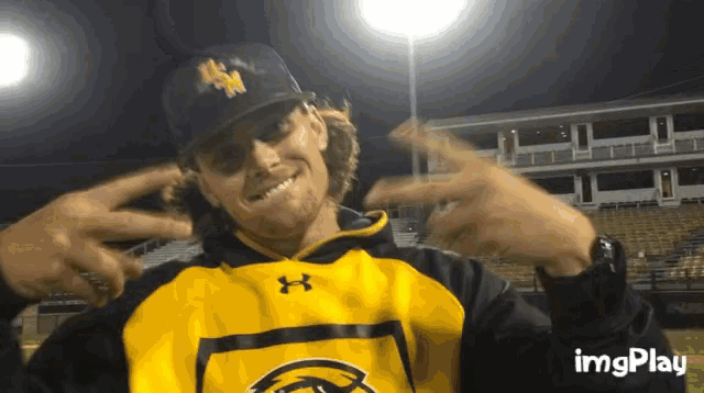 a man wearing a black and yellow under armour hoodie is pointing to his head