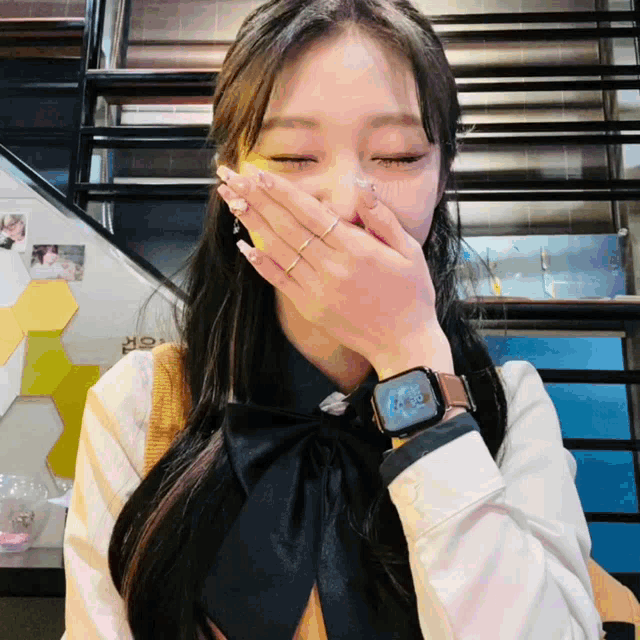 a woman wearing a watch covering her mouth with her hand and a ring on her finger
