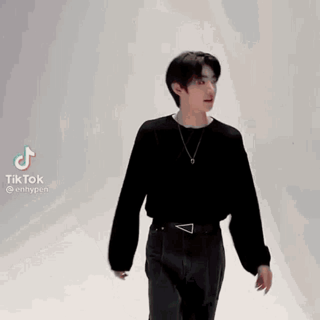 a young man wearing a black sweater and a silver necklace is standing in front of a white wall .