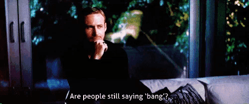 a man is sitting on a couch talking on a cell phone and says are people still saying bang ?