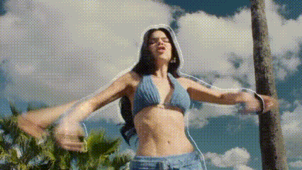 a woman in a bikini and shorts is standing in front of a palm tree with her arms outstretched .
