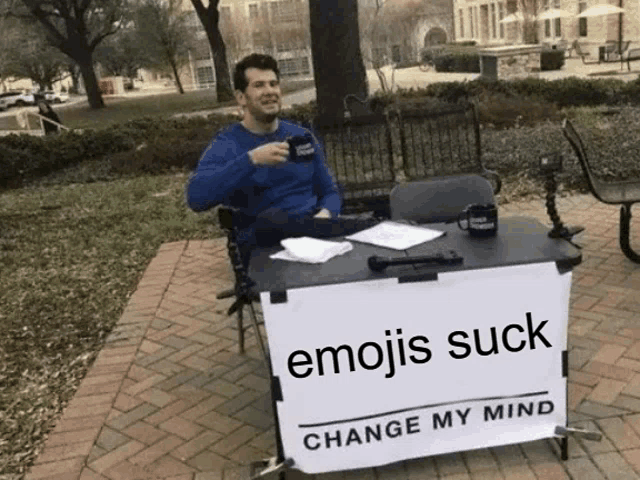 a man sits at a table with a sign that says " emojis suck "