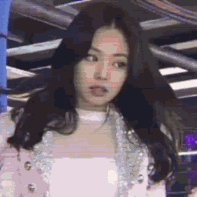 a woman with long black hair is wearing a pink jacket and white top .
