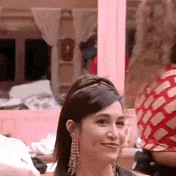 a woman wearing earrings and a headband is smiling in a pink room .