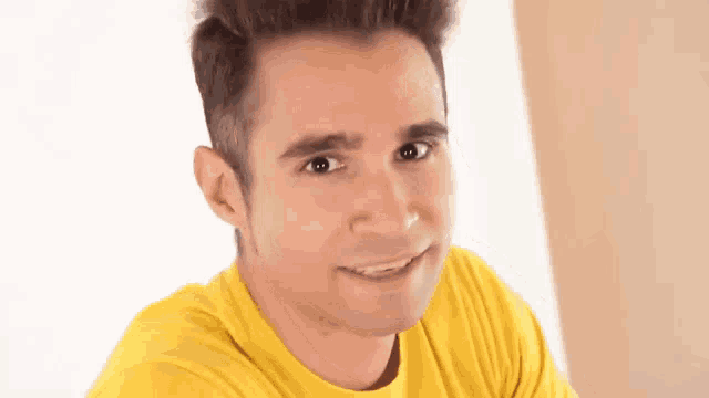 a young man in a yellow shirt is smiling and making a funny face