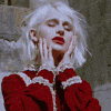 a woman with white hair and red lipstick is wearing a red dress and covering her face with her hands .