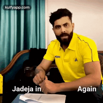 a man with a beard wearing a yellow shirt is sitting at a table with a book .
