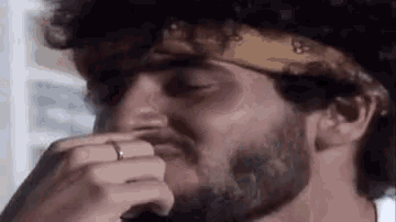 a man with a beard wearing a bandana and a ring on his finger is covering his nose .