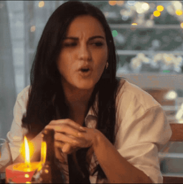 a woman in a white shirt is sitting at a table with a candle in her hand .