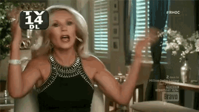 a woman in a black dress is holding a glass of wine in front of a tv screen that says bravo .