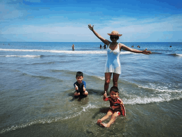 a woman in a white dress stands in the ocean with two children