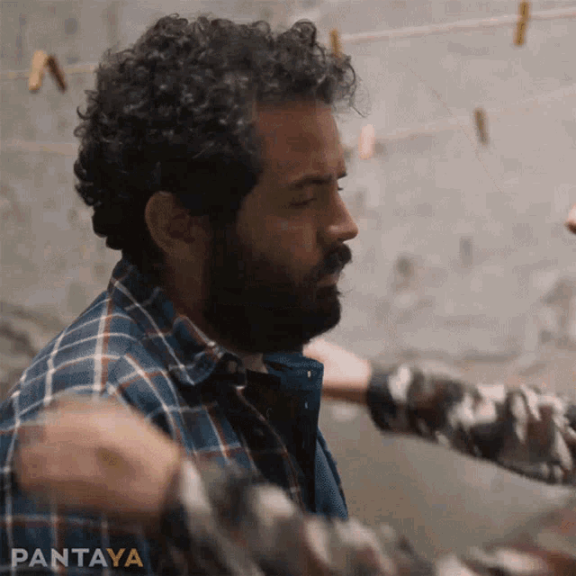 a man with curly hair and a beard in a plaid shirt is being held by another man .