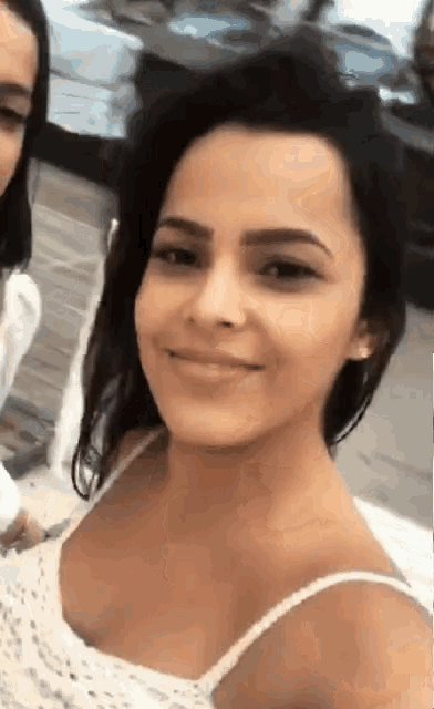 a woman in a white tank top is smiling and looking at the camera