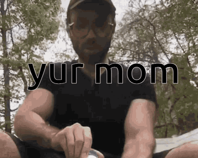 a man wearing glasses and a hat is sitting in front of a sign that says yur mom