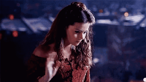 a woman in a red dress is standing in a dark room looking down at something .