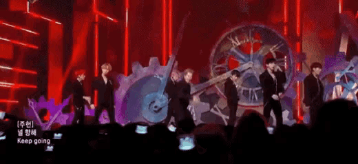 a group of men are dancing on a stage with a large clock in the background ..